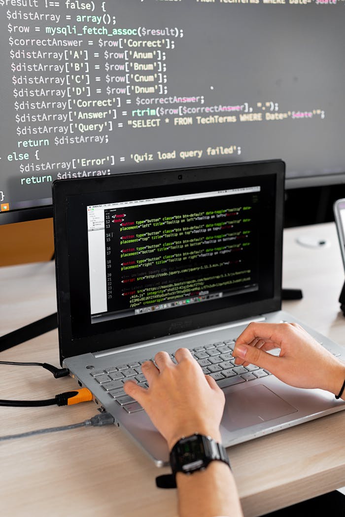 Person coding at a desk with laptop and external monitor showing programming code.